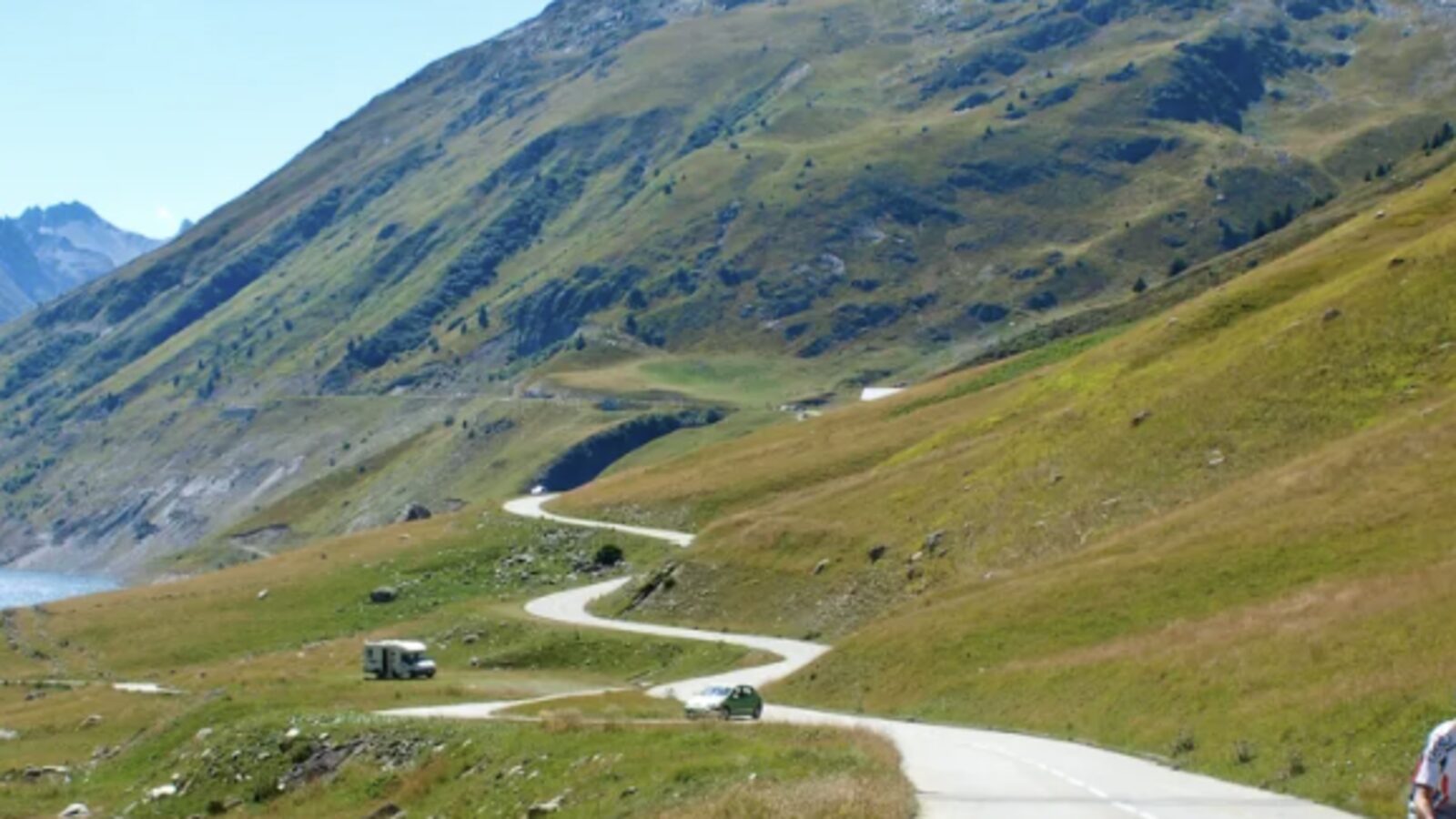 Winding alpine road above Lac de Grand Maison on the Col de la Croix de Fer climb under a clear blue sky