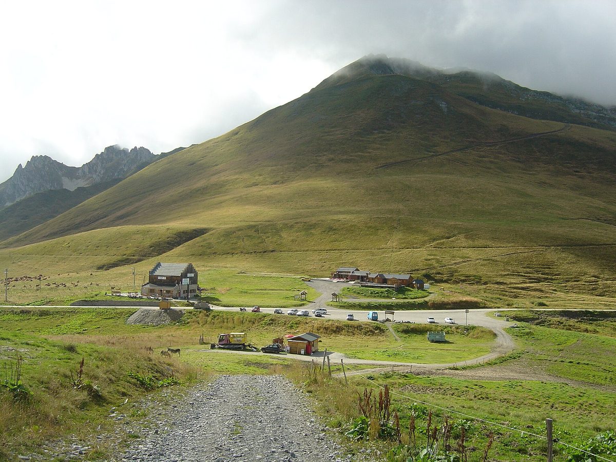 General view of the Col de la Madeleine (1,993 m): green pastures, the summit buildings and a grassy peak under cloud