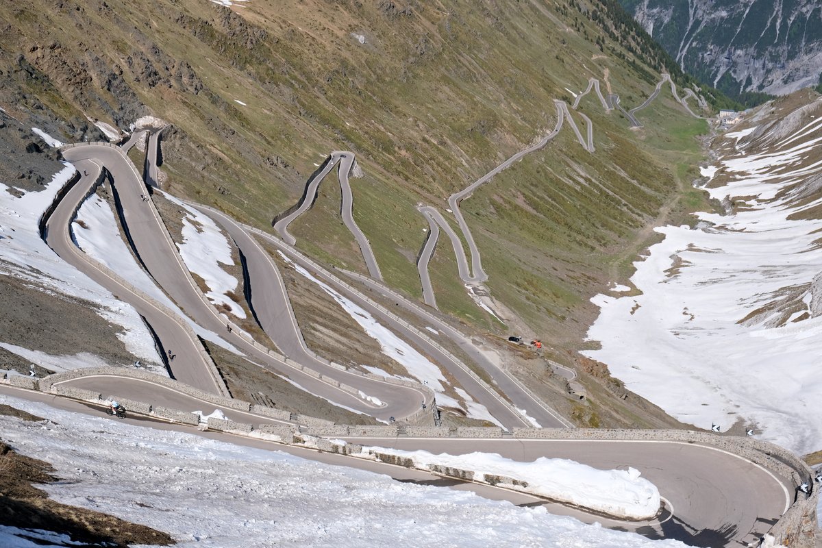 The stacked hairpins of the Stelvio Pass road on the Prato (South Tyrol) side, seen from near the summit, with snow still lying beside the road in late May